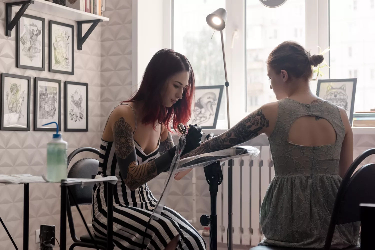 Concentrated stylish artist tattooing hand of young girl sitting in modern studio. 